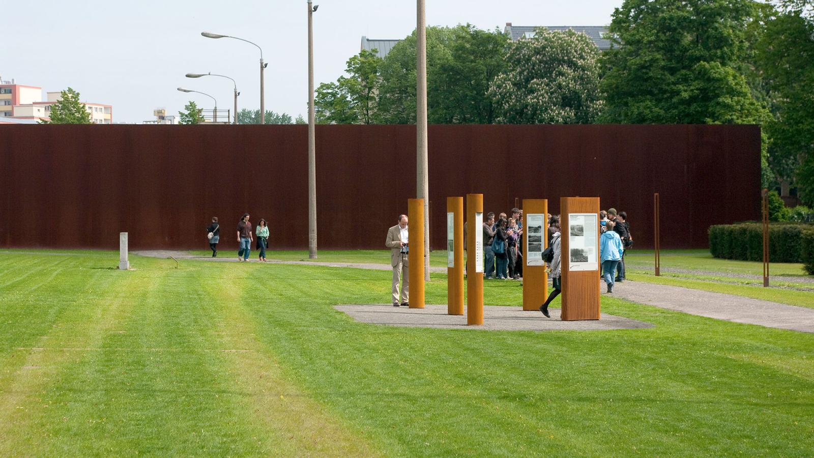 Besuchende auf dem Gelände der Gedenkstätte. Im Hintergrund sieht man die Rückwand des Denkmals