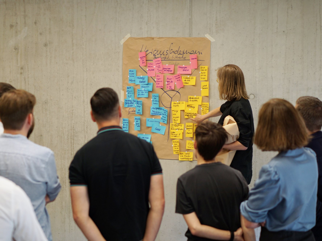 Personen stehen vor einer Tafel mit Klebezetteln